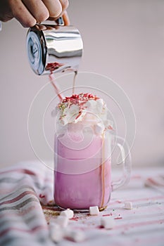 Woman is pouring coffee in stylized mason jar cup of colored milk with cream, marshmallow and colorful decoration. Milk shake, coc