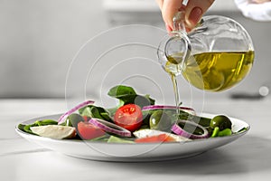 Woman pouring cooking oil onto plate with salad at white table, closeup