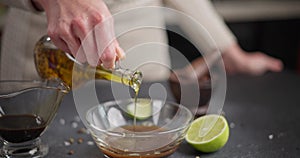 Woman pouring cooking olive oil into glass bowl with teriyaki soy sauce and lime juice preparing marinade