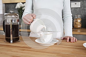 Woman pouring cream into her cup of coffee. Conceptual image