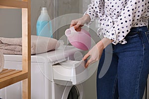Woman pouring detergent into washing machine drawer in bathroom. Laundry day