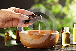 Woman pouring essential oil from glass bottle into bowl on table