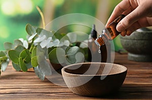 Woman pouring eucalyptus essential oil into bowl on wooden table