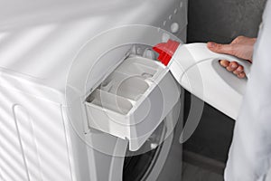 Woman pouring fabric softener from bottle into washing machine indoors, closeup