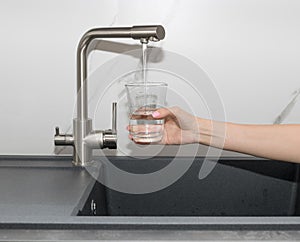 Woman pouring filtered water from tap into glass in kitchen