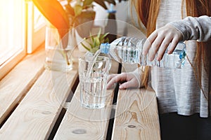 woman pouring fresh drink water from blue plastic bottle inside