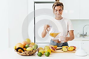 Woman pouring freshly squeezed homemade orange juice into the glass in modern white kitchen