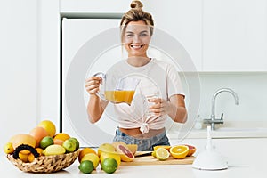 Woman pouring freshly squeezed homemade orange juice into the glass in modern white kitchen