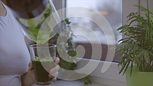 Woman pouring glass of green fresh smoothie in the kitchen