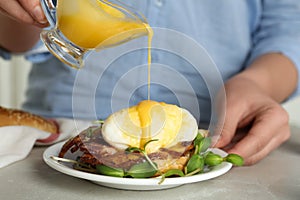 Woman pouring Hollandaise sauce onto egg Benedict at table