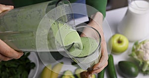 woman pouring homemade fresh green smoothie into a glass, made from healthy vegetables and fruits. healthy lifestyle