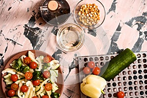 Woman pouring honey mustard dressing into bowl with fresh salad on table