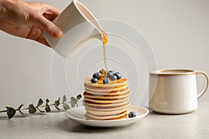 Woman pouring honey onto tasty pancakes with berries