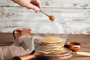 Woman pouring honey on stack of tasty pancakes