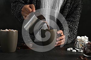 Woman pouring hot chocolate with milk into cup on table