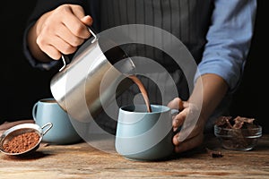 Woman pouring hot cocoa drink into cup on table, closeup