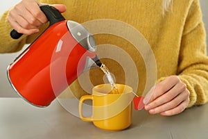 Woman pouring hot water into cup with tea bag at grey table, closeup