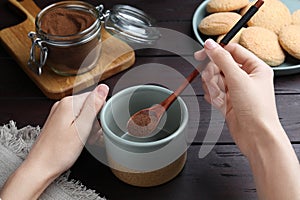 Woman pouring instant coffee into mug at wooden table, closeup