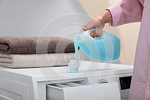 Woman pouring laundry detergent into cap on washing machine indoors