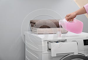 Woman pouring laundry detergent into cap on washing machine indoors, closeup