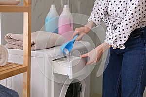 Woman pouring laundry detergent into washing machine drawer in bathroom