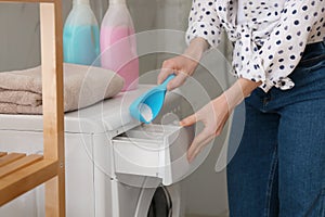 Woman pouring laundry detergent into washing machine drawer in bathroom