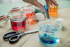 Woman pouring liquid orange Easter cold colour color in glass with water and vinegar next to green, yellow, red, blue dye in