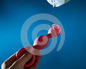 Woman pouring lubricant on pink anal beads on blue background.