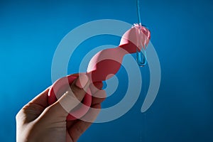 Woman pouring lubricant on pink anal beads on blue background.