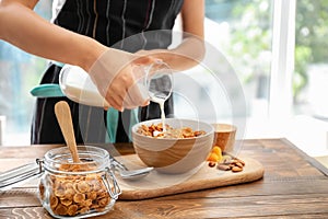 Woman pouring milk into bowl with corn flakes at table