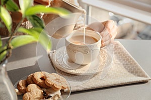 Woman pouring milk into cup with aromatic tea on table