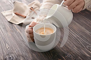 Woman pouring milk into cup of tea on table