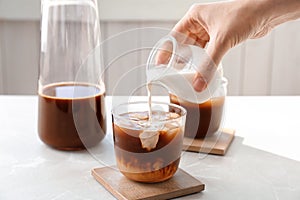 Woman pouring milk into glass with cold brew coffee