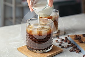 Woman pouring milk into glass with cold brew coffee