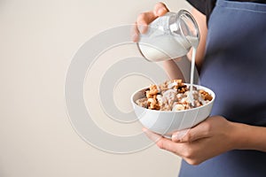 Woman pouring milk from jar into bowl with granola on light background