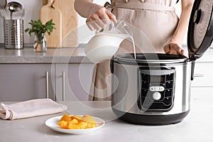 Woman pouring milk into modern multi cooker for making delicious yogurt at table