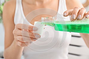 Woman pouring mouthwash from bottle into ca