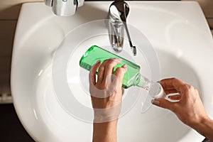 Woman pouring mouthwash from bottle into cap in bathroom, closeup.