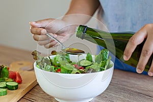 Woman pouring olive oil into  fresh vegetable salad bowl in the kitchen
