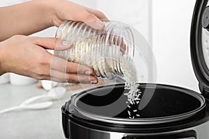 Woman pouring rice from jar into cooker in kitchen