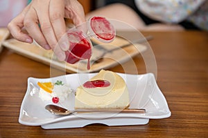 Woman pouring strawberry sauce to cheesecake