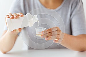 Woman pouring syrup from bottle to medicine cup