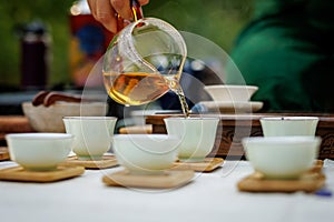 A woman pouring tea in a Chinese tea cup from a glass teapot