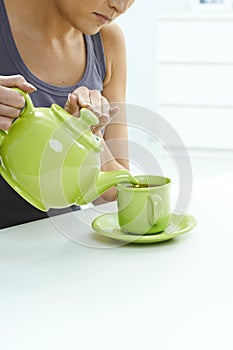 Woman pouring tea from kettle to mug on table