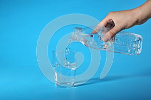 Woman pouring water from bottle into glass on blue background