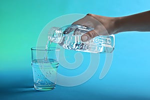 Woman pouring water from bottle into glass on blue background