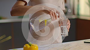 Woman pouring water into glass from jug at home. Girl drinking water on kitchen