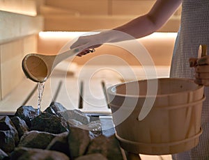 Woman pouring water into hot stone in sauna room