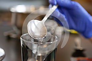 Woman pouring water from metal spoon into glass cup