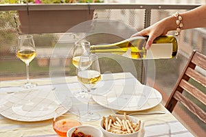 Woman pouring white wine to the wine glasses on the terrace